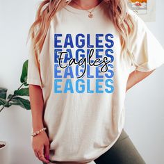 Get this popular new Eagles stacked text shirt and show off your school spirit in style!  Each shirt is printed in-house by me using high-quality materials on a Comfort Colors shirt, known for its exceptional comfort, style, and durability. Available in unisex sizes S to 3X, and youth sizes, we've got you covered regardless of your preferred fit. The Eagles stacked text Shirt features a classic crew neck and short sleeves, making it suitable for year-round wear. The flattering silhouette ensures a comfortable and stylish fit for both men and women. Please note that ivory is ONLY available in Adult sizes!  Note: As each shirt is individually printed, slight variations in color and placement may occur, adding to the uniqueness and charm of your Eagles Shirt. Your shirt will come with care in Blue Top With Name Print For Game Day, Blue Tops With Name Print For Game Day, Eagles Spirit Wear, Blue School Spirit T-shirt With Text Print, Blue School Tops With Team Name, Blue College T-shirt With Name Print, Team Spirit Graphic T-shirt For School, Blue School Spirit T-shirt With Heat Transfer Vinyl, Team Spirit Graphic Print School T-shirt