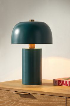 a green lamp sitting on top of a wooden table next to a box and a book