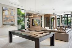 a pool table in the middle of a living room with couches and large windows