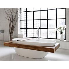 a large white bath tub sitting in front of a window next to a vase with flowers