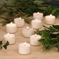 white candles are arranged on a table with greenery