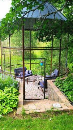 a gazebo in the middle of a garden surrounded by greenery and bushes with blue chairs