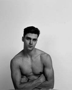 black and white photograph of a shirtless man sitting at a table with his arms crossed