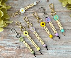 six keychains with flowers and beads on them sitting on a wooden table next to green leaves