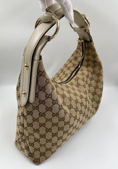 A stunning vintage Gucci hobo bag made from the iconic beige GG canvas with cream leather trim and pale gold hardware. Inside the bag is lined with a brown cotton lining and there is a zipped pocket for valuables. This bag is in excellent vintage condition, a true collectors item and comes with its original Gucci dust bag. There is some slight wear seen on the base corners. Gucci Hobo Bag, Gucci Horsebit, Pale Gold, Exclusive Bag, Vuitton Bag, Diaper Backpack, Flap Bag, New Bag, Hobo Bag