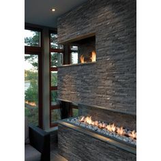 a modern fireplace in the middle of a living room with large windows and stone walls