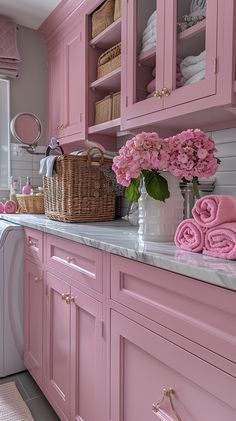 a bathroom with pink cabinets and flowers on the counter top, along with white towels