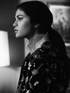 a black and white photo of a woman sitting in front of a lamp looking off into the distance