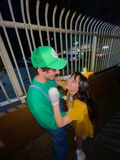 a man and woman dressed up as mario and luigi in front of a white fence