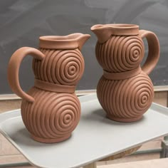 two brown vases sitting on top of a white tray