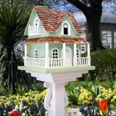 a bird house on top of a white pedestal in front of some flowers and trees