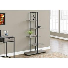 a black and silver book shelf next to a desk with a plant on it in front of a gray wall