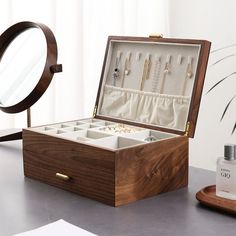 an open wooden jewelry box sitting on top of a table next to a mirror and other items