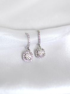 These earrings showcase a breathtaking round brilliant moissanite in centre stage, surrounded by a sparkle cut finish and a dazzling halo of cubic zirconia diamond simulant side stones. ♥ Material: 925 sterling silver with 14K white gold plating ♥ Gem: D VVS1 0.5 carat (5mm) moissanite centre stone with total carat weight of 1 carat  ♥ Size: Hoop inner diameter of 9mm ♥ Packaging: Comes in a pink jewellery box packaging ♥ Warranty: Covered by Clair Moissanite Warranty (limited lifetime warranty on moissanite gemstone) and Clair Jewellery Warranty (one year standard warranty) Read more about us at www.clairlondon.co.uk Elegant Cubic Zirconia Halo Diamond Earrings, Elegant Halo Cubic Zirconia Diamond Earrings, Diamond White Halo Earrings In Cubic Zirconia, Halo Diamond White Earrings In Cubic Zirconia, Dazzling Diamond Halo Cluster Earrings, Dazzling Diamond Cluster Earrings With Halo, Cubic Zirconia Round Cut Cluster Earrings For Wedding, Dazzling Diamond White Halo Diamond Earrings, Dazzling Halo Diamond White Diamond Earrings