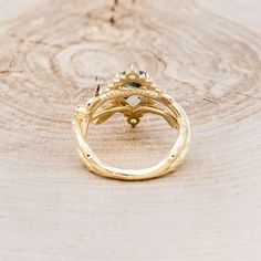 a close up of a gold ring on top of a piece of wood with green stones