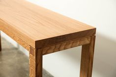 a wooden bench sitting on top of a floor next to a white wall and cement floor