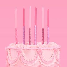 a birthday cake with pink frosting and lit candles on top, in front of a pink background