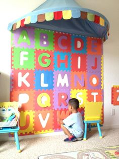 a young boy sitting on the floor in front of a colorful wall with letters and numbers