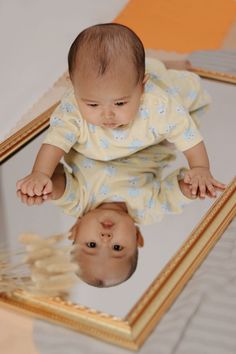 a baby looking at itself in a mirror with its reflection on the floor next to it