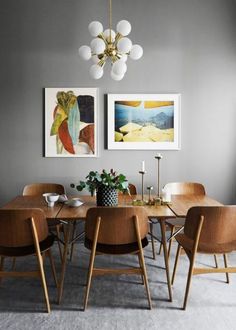 a dining room table with chairs and pictures on the wall above it, along with two paintings