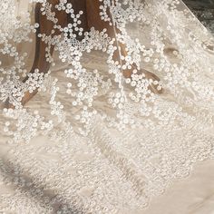 an embroidered white dress with flowers on it and sheer fabric over the top, hanging from a wooden stand