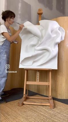 a woman is painting on an easel with white cloth