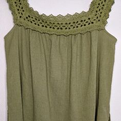 a green top with crochet on the neckline hanging up against a white wall