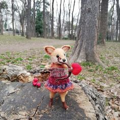 a stuffed animal with a knitted sweater and red mittens is on a rock in the woods