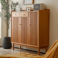 a wooden cabinet sitting in the corner of a living room next to a potted plant