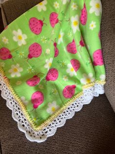 a green blanket with pink and white flowers on it sitting on top of a couch