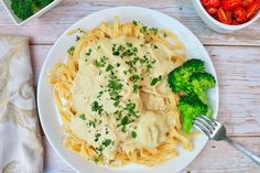 a white plate topped with pasta and broccoli next to a bowl of tomatoes