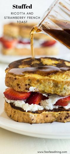 someone is pouring syrup on a french toast sandwich with strawberries and goat cheese in the foreground