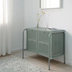 a green sideboard with two drawers and a plant on top in front of a window