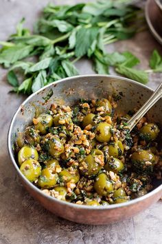 a metal bowl filled with green olives and breadcrumbs next to some parsley