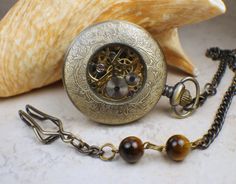 "Men's mechanical pocket watch in bronze with skull and crossbones mounted on front cover of pocket watch. The skull and crossbones have been sealed with a clear resin to give a mirror like finish. The chain is a traditional clip chain and is 13\" in length and has beads adorning it. The watch has a black dial featuring silver numerals. This is a mechanical self wind watch that needs no batteries. The watch case is a rich bronze and front cover opens to reveal watch face, you can see the gold co Steampunk Pocket Watch With Metal Dial As Gift, Steampunk Style Pocket Watch With Metal Dial As Gift, Steampunk Pocket Watch With Metal Dial, Steampunk Style Metal Dial Pocket Watch For Gift, Steampunk Pocket Watch With Compass Design, Steampunk Bronze Pocket Watch Gift, Steampunk Bronze Pocket Watch With Locket, Bronze Steampunk Pocket Watch With Locket, Steampunk Engraved Pocket Watch As Gift