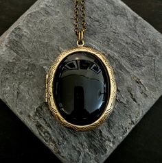 Rich black onyx framed in antiqued brass. Locket opens with 2 spaces for pictures or things. Locket hangs from long antiqued brass chain.  Details: Locket measures 45mm x35mm Locket and chain are plated brass Necklace measures 28 inches Lead and nickel free Stone is genuine onyx Please allow for possible slight color differences due to different settings on different screens. Thank you for shopping Delicate Industry :) Black Brass Round Pendant Jewelry, Black Engraved Brass Necklaces, Vintage Black Oval Pendant Jewelry, Black Brass Medallion Jewelry, Black Medallion Locket Necklace As A Gift, Vintage Black Locket Necklace, Elegant Black Pendant Locket Necklace, Black Medallion Necklace With Vintage Charm, Victorian Oval Brass Locket Necklace