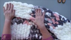 a woman is holding up a blanket made out of knitted wool and yarn balls