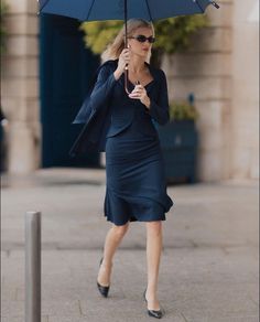 a woman is walking down the street with an umbrella in her hand and she is wearing a blue dress