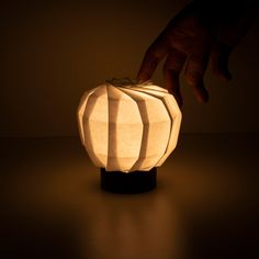 a hand reaching for a paper lantern that is lit up on a dark table top