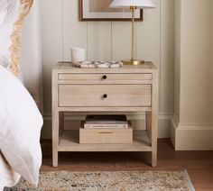 a nightstand with a lamp on top of it next to a bed and a rug