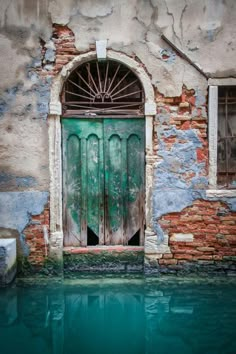 an old building with a green door next to a body of water in front of it