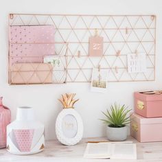 a desk with pink and gold decor on the wall, including pineapples in vases