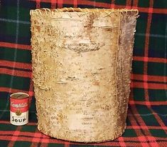 a tin can sitting on top of a plaid blanket next to a metal cup with a lid