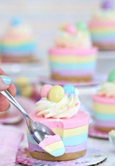 a person holding a spoon over a piece of cake with pastel icing on it