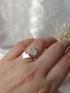 a person's hand with a ring on it and a flower in the background