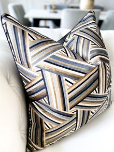 a white couch with a blue and gold pillow on it's backrest in front of a dining room table