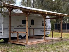 an rv is parked in the grass under a wooden structure with a porch attached to it