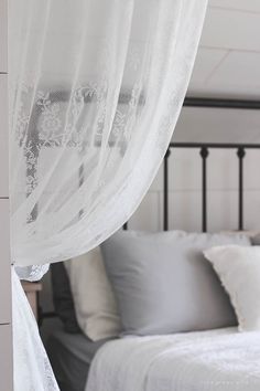 a white bed sitting next to a window covered in sheer curtains