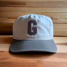 The varsity cap was created as homage to the letterman days. We took the style of the 90's unstructured flat-bill snapbacks and the varsity jacket and threw a modern twist of our "G" on there to represent the lifestyle of Genuine. It sports a mid profile crown to fit more standard than our previous hats. This two toned walnut and natural cap is our new go to. Retro Adjustable Snapback Hat For Sports, Retro Fitted Hat For Baseball Season, Retro Flat Brim Snapback Hat For Baseball Season, Retro Adjustable Fitted Hat For Baseball Season, College Baseball Cap With Flat Brim For Baseball Season, College Baseball Season Flat Brim Cap, College Baseball Season Flat Bill Cap, Retro Embroidered Logo Snapback Hat For Streetwear, Retro Embroidered Logo Snapback Baseball Cap