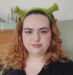 a woman with red hair wearing a green knitted devil's horns headband